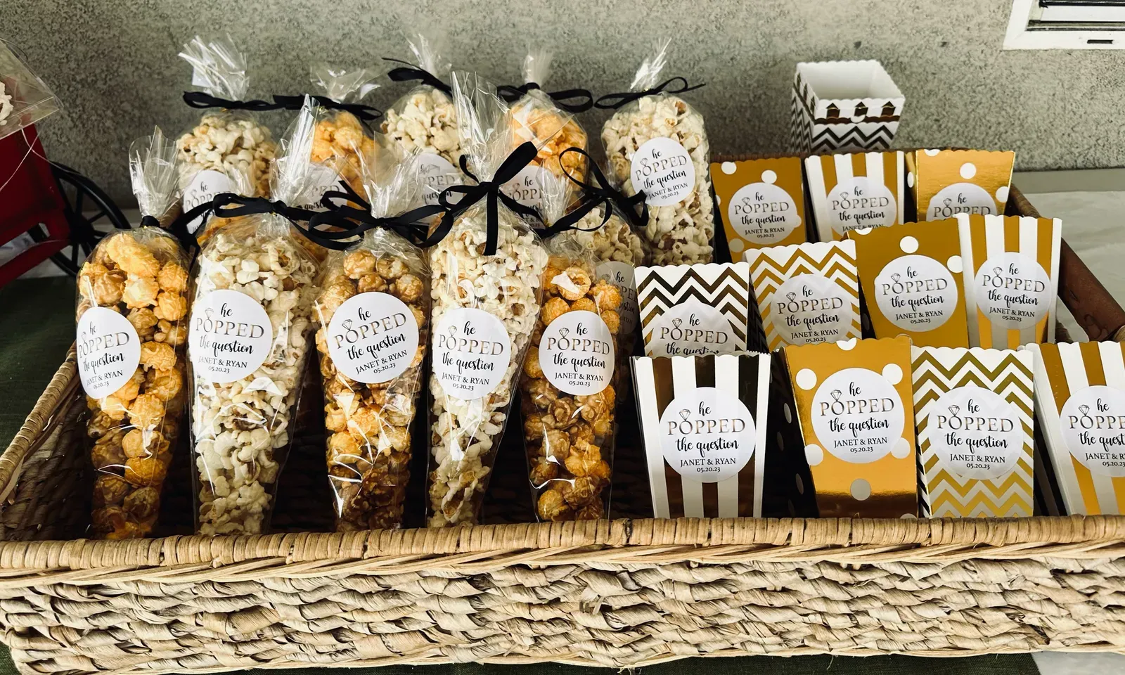 Engagement party popcorn favors in printed cones and boxes, tied with black ribbon in a woven basket