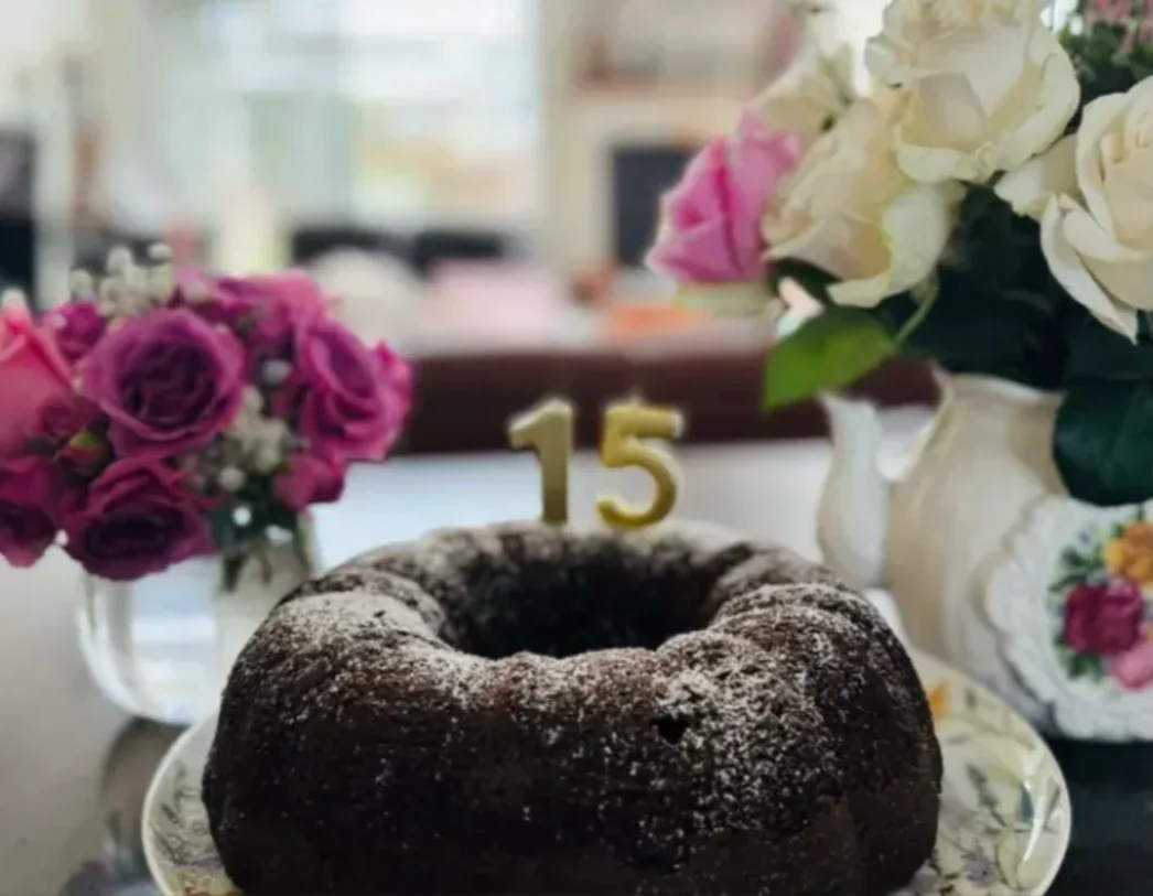 Gluten-free chocolate bundt cake with a gold number candle, framed by pink and white roses on vintage china